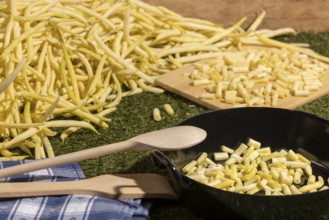 Pan with sliced yellow runner beans and a wooden spoon, beans in the background