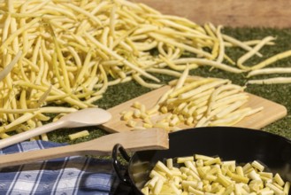 Yellow runner beans next to a cooking pot with sliced beans and wooden spoons