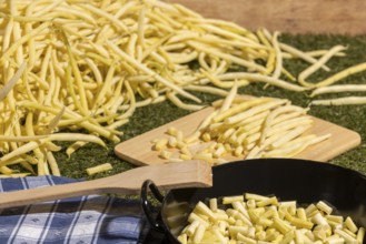 Yellow runner beans next to a cooking pot with sliced beans, with a wooden spoon on top