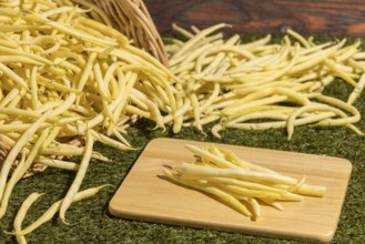 Basket with yellow beans on green grass, some beans on a board
