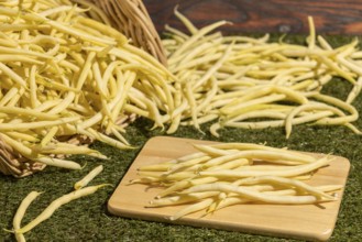 A basket of yellow beans, some on a board on a green background