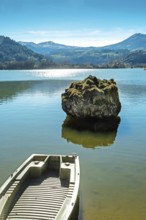 Lake chambon reflects the stunning blue sky and surrounding mountains. A small boat rests at the