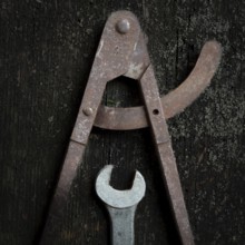 Two old metal tools, a caliper and adjustable wrench, lay on a textured wooden surface, revealing