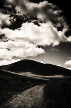 A winding path leads towards a dark mountain silhouette against a dramatic sky filled with
