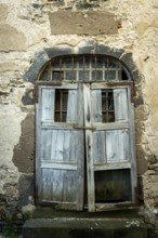 A rustic wooden door stands ajar in an aged stone wall, showing signs of weathering and decay. The