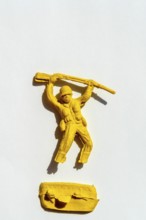 A bright yellow toy soldier holds a rifle above his head, showcasing an imposing stance. The figure