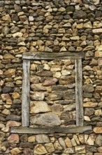 A wall constructed of unevenly arranged stones features a striking wooden frame that outlines an