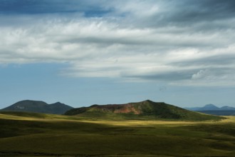 Mountains stretch across the landscape under a vast sky filled with dynamic clouds. Sancy Massif in