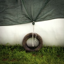 A weathered tire is tied to a green tarp, providing stability in a subtle, serene outdoor setting.