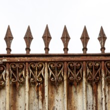 An old, weathered wrought iron fence features intricate scrollwork and pointed spikes atop its