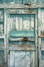 The weathered wooden door features peeling teal paint and rough textures, showcasing its rustic
