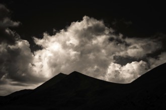 Majestic mountains form a dark outline against a backdrop of swirling clouds illuminated by