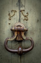 An old, rusty door knocker rests on a weathered wooden door, showcasing intricate designs and the