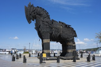 Wooden sculpture of a horse at the harbour in a clear, sunny environment with boats and clouds,