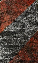 A close-up view of a textured pavement featuring bold diagonal stripes in red and black, showcasing