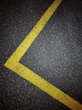 Bright yellow line marking outlines the dimensions of a parking space on a dark asphalt surface in