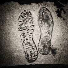 Uniquely patterned shoe prints are visible on a wet concrete surface, showcasing the intricate
