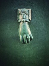 A unique green hand-shaped door knocker adorns a textured dark wall, adding a charming historical