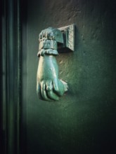 A distinctive bronze hand-shaped door knocker is mounted on a teal door, reflecting intricate