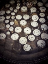 A variety of vintage pocket watches are arranged neatly on a reflective surface in an antique shop,