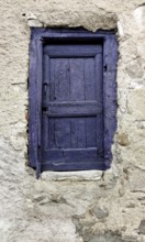 A small door painted in vibrant purple contrasts beautifully with a weathered stone wall. The