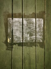 A rectangular patch on a green wooden surface shows faded remnants of a past application, with