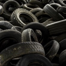 A large collection of worn-out tires is stacked chaotically in a junkyard, illustrating the