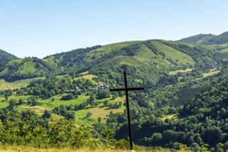 A wooden cross stands prominently against a picturesque landscape of rolling hills and vibrant