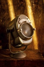 A vintage spotlight rests on a rustic wooden surface, casting a warm glow. Soft light enhances the
