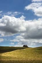 Ruined stone cottage stands alone on a grassy hillside under a partly cloudy sky in a remote