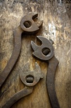 Three antique adjustable wrenches rest on a weathered wooden table, highlighting their unique