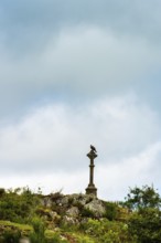 A stone cross towers over rocky ground, surrounded by greenery. Dark clouds loom overhead, creating