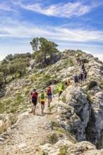 Group of people hiking on a rocky trail high up in the mountains a hot sunny summer day, Mallorca,