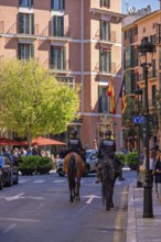 Mounted police on horses on a city street with houses in Palma city with walking tourists on the