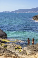 Young women standing in the water by a rocky beach by the sea a sunny summer day, Mallorca, Spain