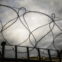 Rusty barbed wire coils twist against a dark and turbulent sky, creating a sense of confinement and