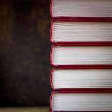 Books are stacked vertically, showcasing their red spines and crisp white pages against a deep
