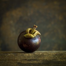 A ripe mangosteen sits gracefully on a weathered wooden surface, showcasing its dark purple skin