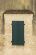 The facade features a pair of blue-green wooden shutters on a weathered wall, showcasing texture