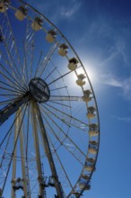 Bright sun shines behind a towering Ferris wheel, creating a vibrant atmosphere at an amusement