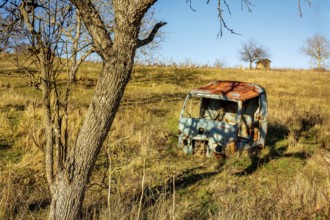 A weathered vehicle rests in a secluded field in Auvergne-Rhone-Alpes, France. Surrounded by tall