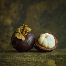 Two ripe mangosteens rest side by side, showcasing their deep purple skin. One fruit is cut in