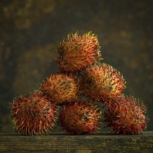 A cluster of rambutans sits on a wooden surface, highlighting their unique hairy skin and rich