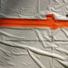 Bright orange tape stretches across a wrinkled white surface, creating a clear boundary. This setup