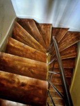 A wooden spiral staircase descends into a bright lower level, showcasing rich grain patterns and a