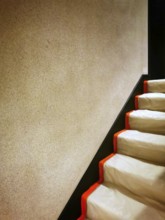 A staircase featuring smooth, soft white steps contrasted by bold orange edges. The surrounding