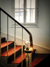 A staircase is gracefully illuminated by a soft light bulb on the railing, leading upward with a