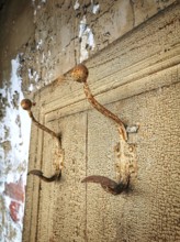 Rusty hooks attached to a weathered wall in a dilapidated building showcasing decay and abandonment