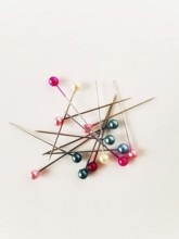 Various sewing pins with colorful heads are scattered across a light background, illustrating the