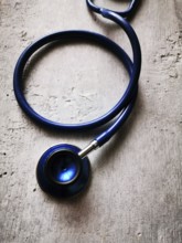 A blue stethoscope lies on a textured surface, its reflection catching the light in a clinical